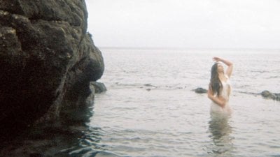 A person posing in the sea with water up to their waist with rocks on the left