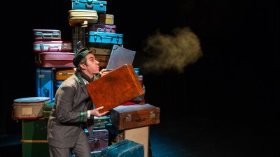 A person stood in front of a big pile of suitcase blowing dust off on one into the distance