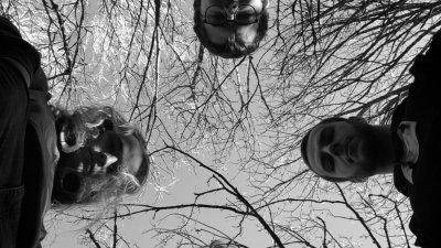 Four musicians looking down at the camera with black and white trees above them