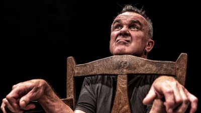 A man pulling a silly afce looking with chin resting on a chair