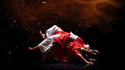 Two dancers performing in white and red outfits with a dark and moody black and red background