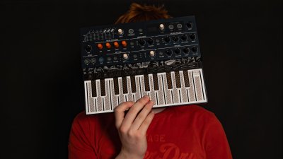 A person wearing a red t-short holding a small midi keyboard in front of their face