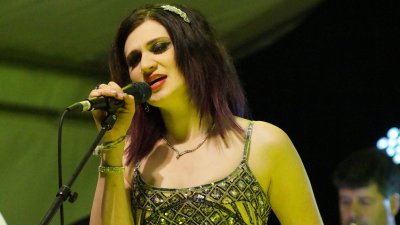 A female singer holding a microphone whilst performing with a green lit background