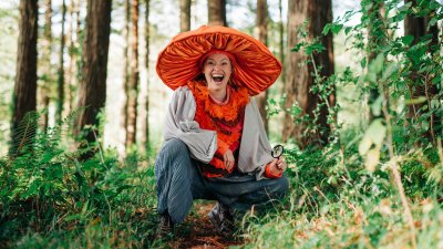 A person in the woods with a large orange fabric mushroom hat on