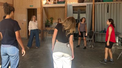 A group of performers in a theatre workshop anwooden room with a green floor
