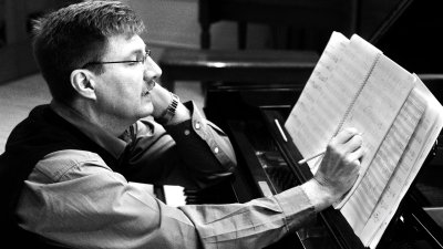 A black and white photo of a composer sat at a piano
