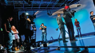 Film studio with people operating cameras against blue background
