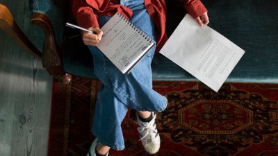 An aerial photo of a girl sat on a sofa with a notebook on her lap and a piece of paper next to her 