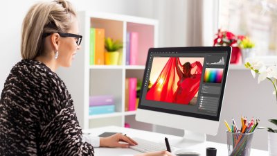A woman working on an iMac editing a photograph of a woman in a red shawl