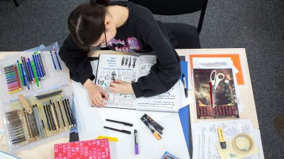 A female student drawing in a sketchbook surrounded by stationary