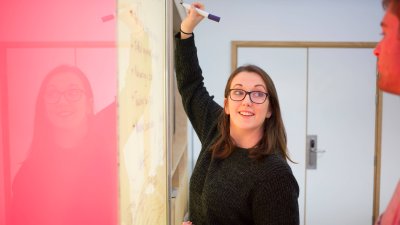 Student writing on a vibrant pink and yellow wall board, Falmouth University