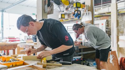 A couple of people working with wood at workshop benches