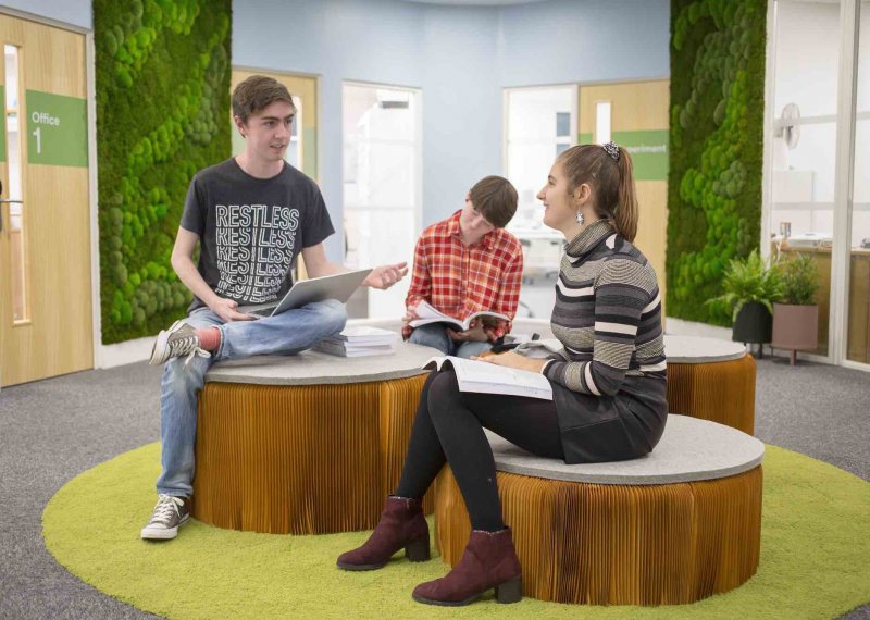 Three Business students sitting on brown seats, talking