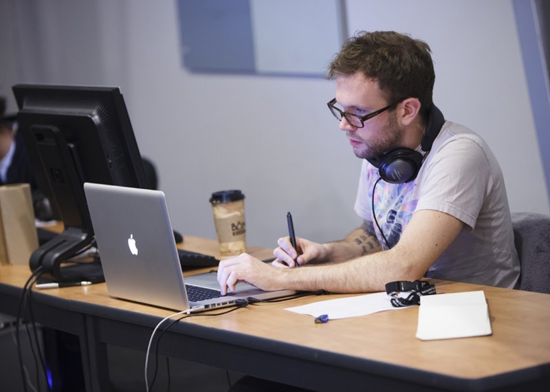 Student with earphones around neck working on graphics tablet.