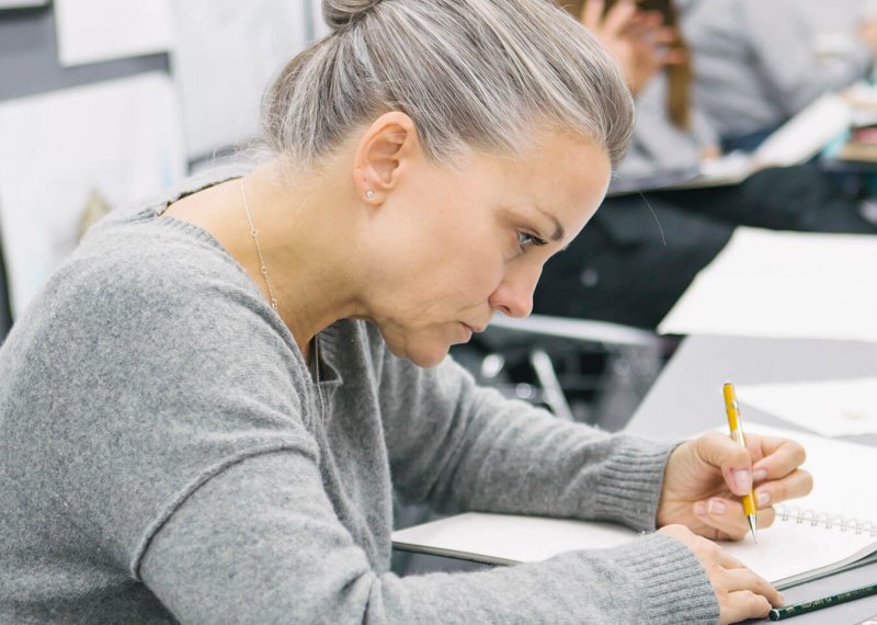 Woman with grey hair and grey jumper writing in a notebook