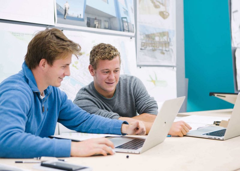 Two male students seated while looking at a laptop