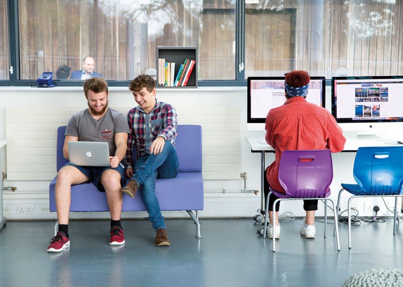 Three business management students working at a laptop and desktop