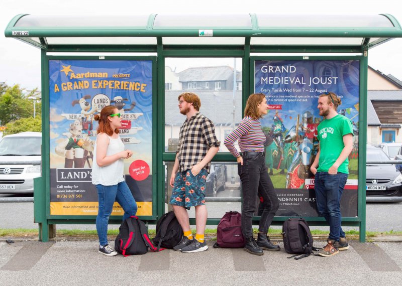 Students stood at bus stop leaning and chatting.