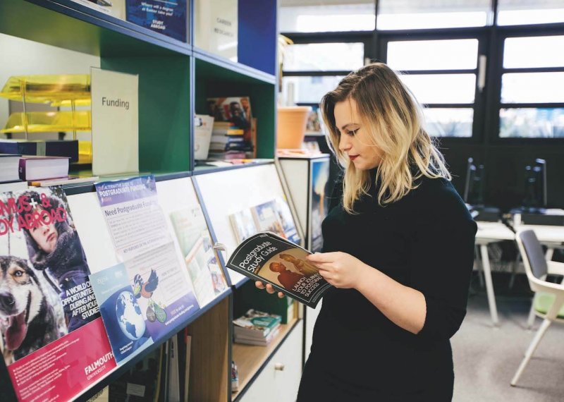 A Falmouth University student looking through a Postgraduate study guide