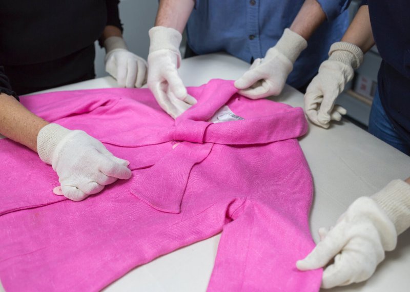 A bright pink jacket with gloved hands touching the garment