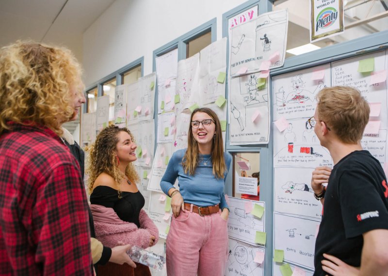 Creative advertising students discussing in front of an ideas wall.