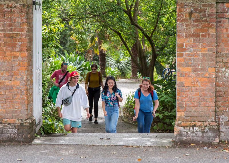 Students walking towards a gateway between red brick walls on Falmouth campus.