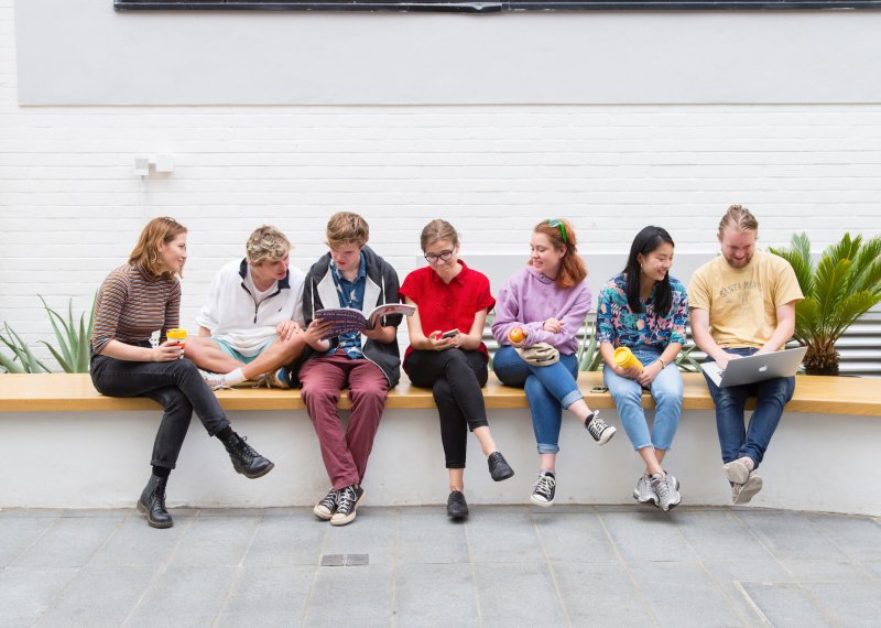 A group of Falmouth University students sitting on a wall inside a white building