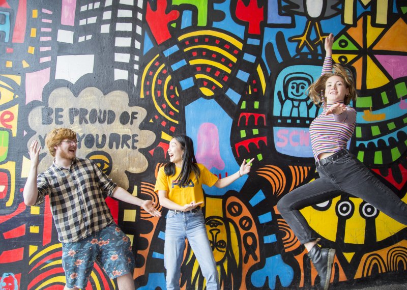 Students jumping in front of brightly coloured mural.