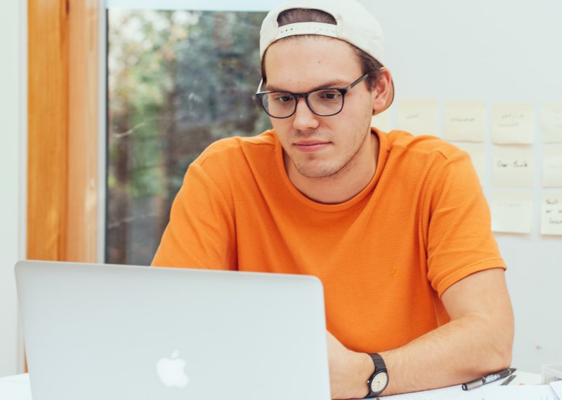 Student in orange t-shirt working on a MacBook.