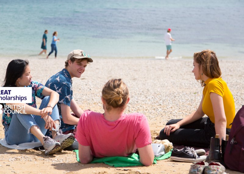 Students sitting on a beach with GREAT scholarship and British Council logo overlaid