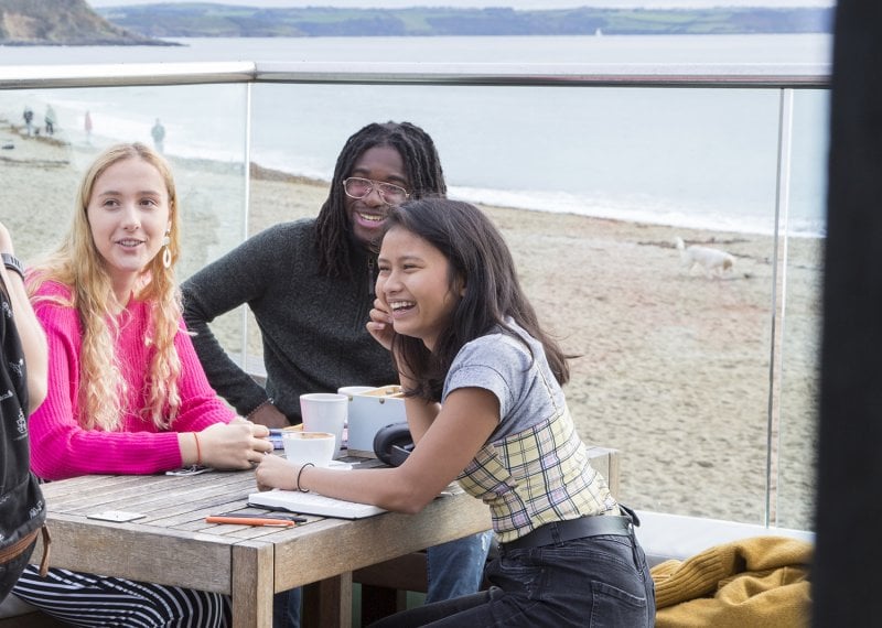 students sat outside on a bench overlooking the sea