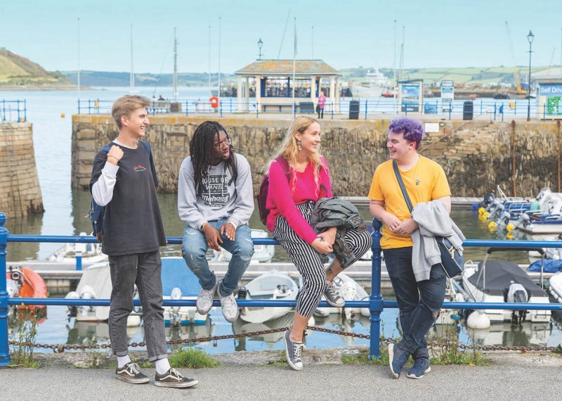 Falmouth University students sitting by the harbour on a sunny day