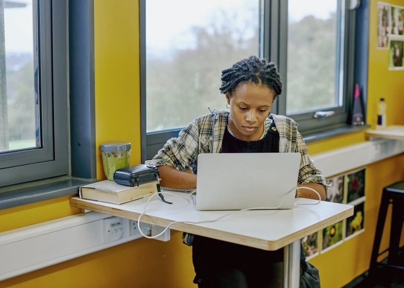 A student sat at a table with a laptop and yellow walls