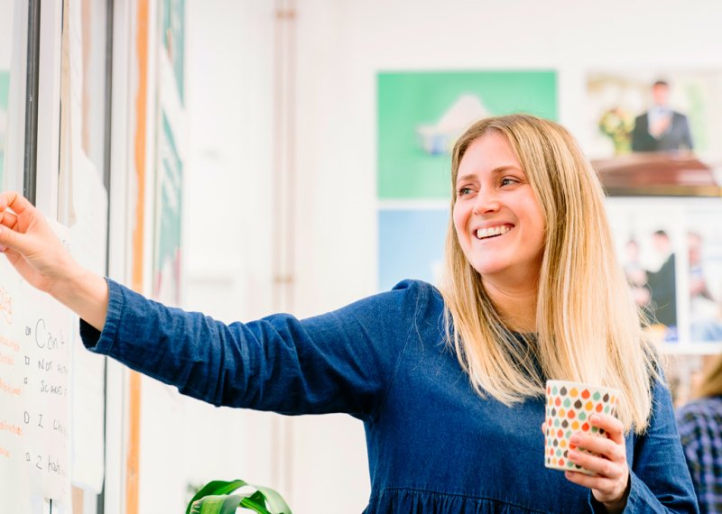 A woman with blonde hair and a blue dress, smiling and putting paper on a board