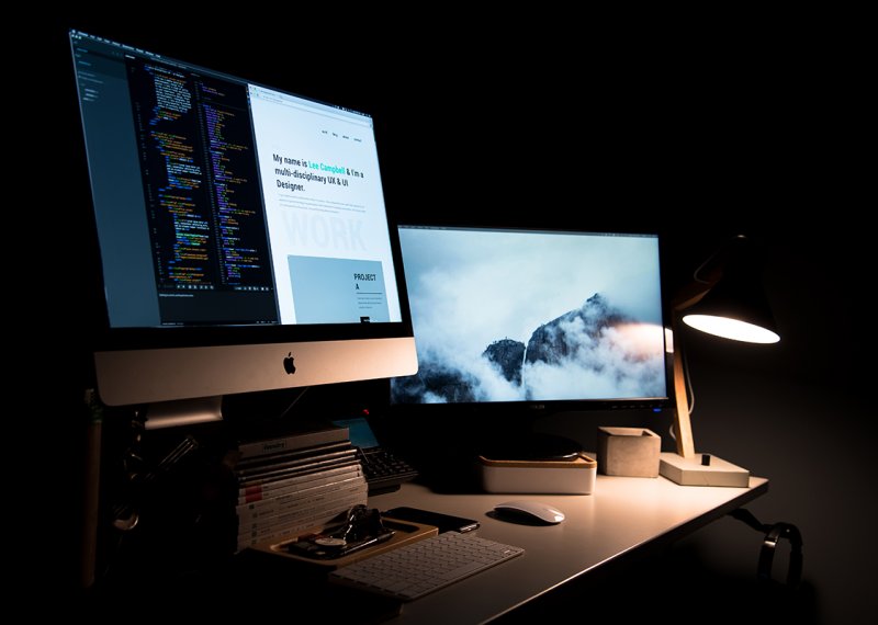 Desktop screens lit up in a dark room.