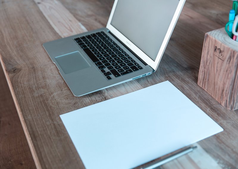 Laptop on a desk with some paper arranged next to it.