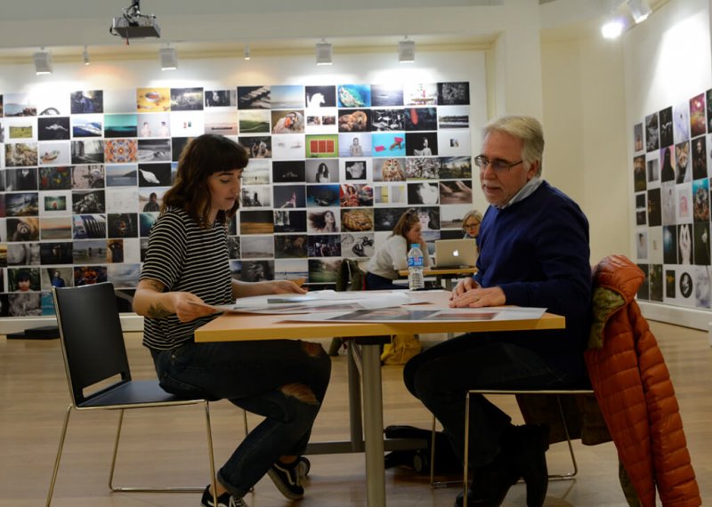 A student and lecturer sat at a table with a photo montage on the wall