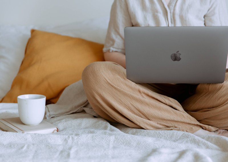 A person sat crossed legs with an apple mac and a cup