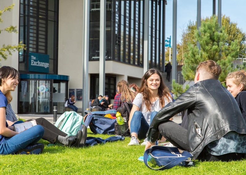 Penryn campus students outside exchange, sitting on grass
