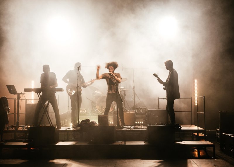 Shadowy figures of a four piece band playing on a smokey stage.