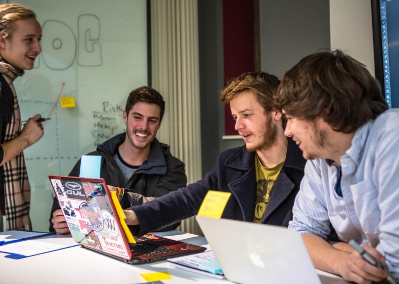 Falmouth University Business students smiling and looking at a laptop