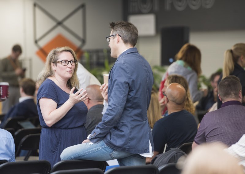 A man and a woman standing and talking in a room full of people