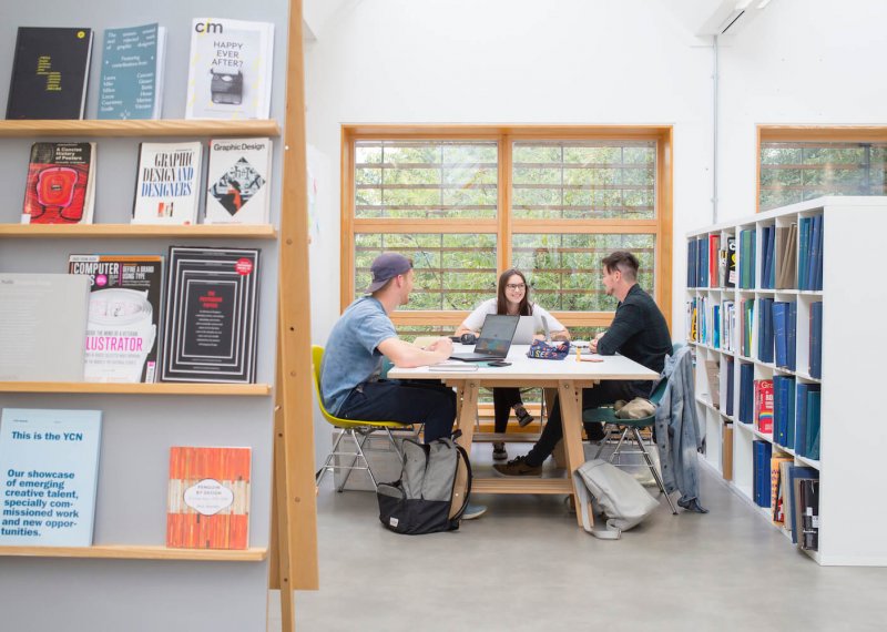 Three students sat at a table in a Graphic Design studio at Falmouth University