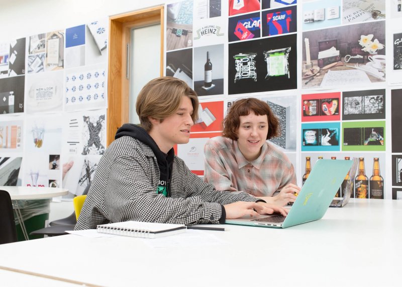 Two Falmouth University students working together at a laptop in a graphic design studio 
