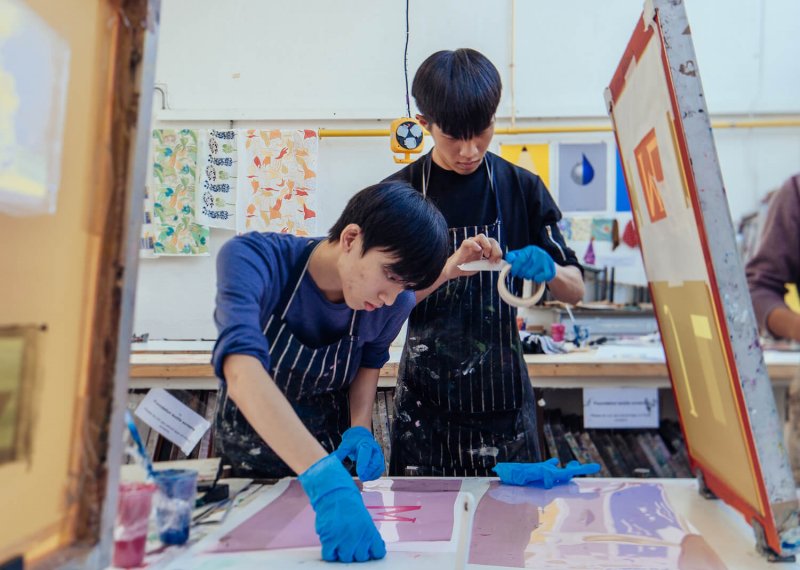 Two Falmouth University Graphic Design students screen printing in a studio