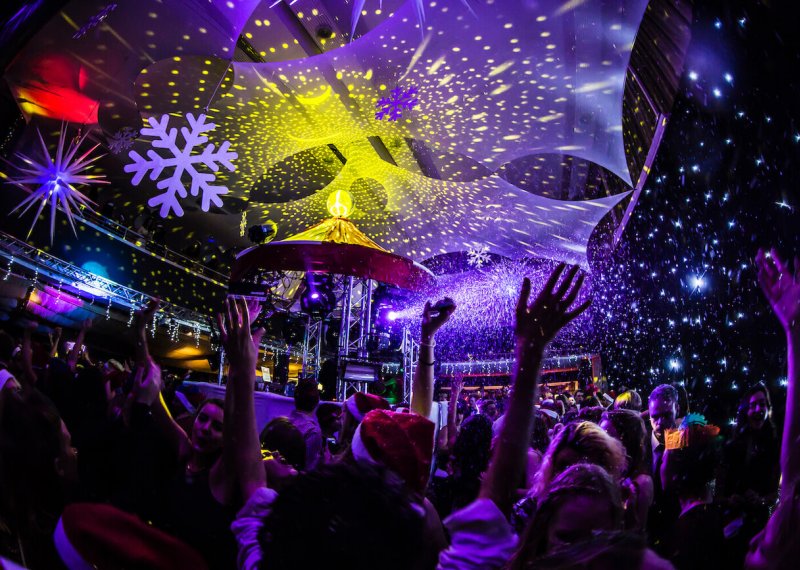 Dark room with disco lights and students dancing with arms in the air.