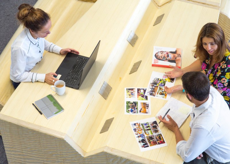 Two women and a man seated at a desk with a laptop and print outs