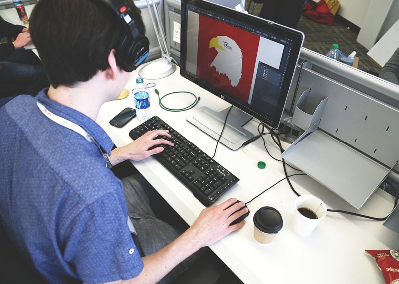 Student with headphones on working on InDesign at a desktop.