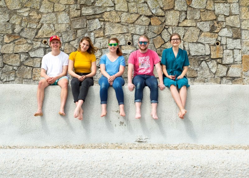 Barefooted students sitting on a wall at the beach.