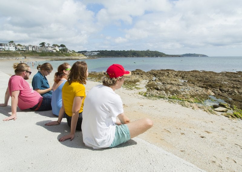 Falmouth students sat on a wall at the Gyllingvase beach looking out to sea.